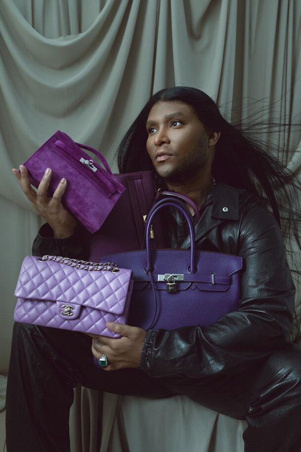 Law Roach holding a purple Chanel double flap bag, a purple suede Hermes Kelly Pochette, a purple Hermes Kelly and a purple Hermes Birkin bag