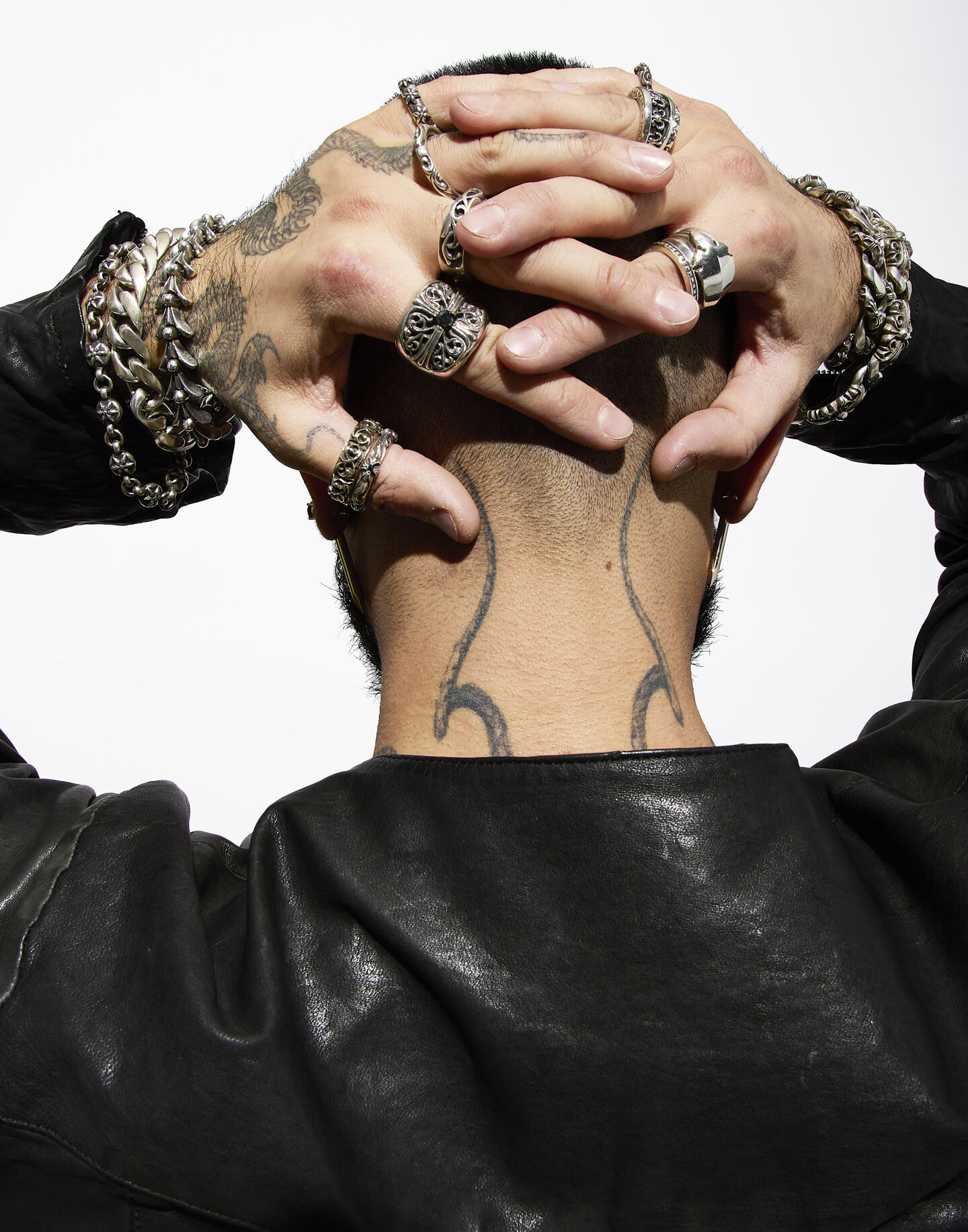 Model with his hands on head wearing Chrome Hearts rings and bracelets.