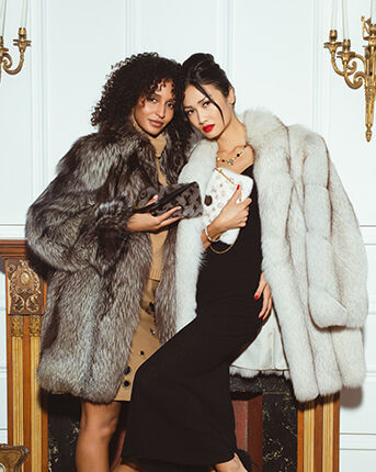 About Us: Two models in fur coats one of them is a holding a Louis Vuitton grey mink Milla shoulder bag and the other a Louis Vuitton white mink Neopochette Milla bag.