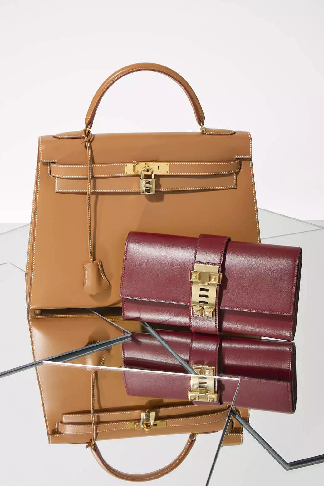 Shop by Brand: Hermes Gold Box Leather Kelly 25 with a Hermes burgundy box leather Medor clutch on a mirrored surface