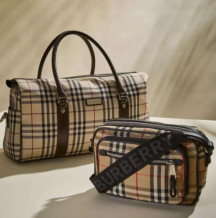 Burberry Edit: Two Burberry plaid bags displayed on a cream backdrop, featuring a structured top-handle bag in the back and a smaller belt bag with a black Burberry logo strap in front.