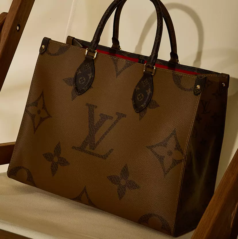 Louis Vuitton Feature: Louis Vuitton monogram tote bag displayed on a cream canvas chair with a wooden frame, featuring dark top handles and a structured silhouette.